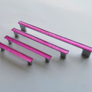 Fired glass cabinet pulls in sparkly bright pink made of fine glass sticks attached over a metal base. Slightly textured glass furniture handles with rounded edges.