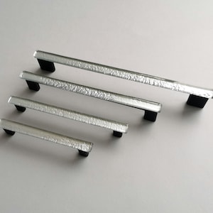 May include: Four silver glass cabinet door pulls with black metal end caps. The pulls are arranged in descending order of size.