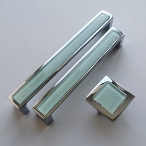 Puede incluir: Dos tiradores de armario plateados con un inserto de vidrio azul claro y un pomo cuadrado a juego con un inserto de vidrio azul claro.