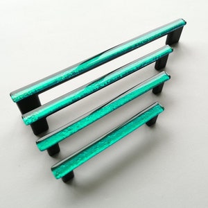 May include: Four turquoise glass cabinet pulls with black metal bases. The pulls are arranged in a staggered pattern, with the largest pull at the top and the smallest pull at the bottom.