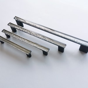 May include: Four silver glass cabinet pulls with black metal bases. The pulls are arranged in order of size, with the largest pull at the top and the smallest pull at the bottom.