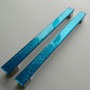 May include: Two turquoise blue glass cabinet door pulls with a textured finish and silver metal mounting plates.
