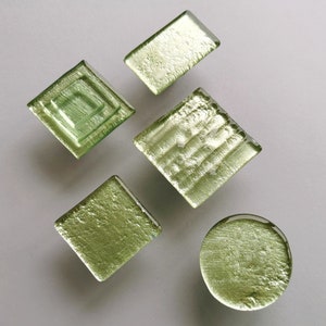 Peut inclure: Cinq carreaux de verre vert avec différentes textures et motifs. Les carreaux sont disposés de manière aléatoire sur un fond blanc.
