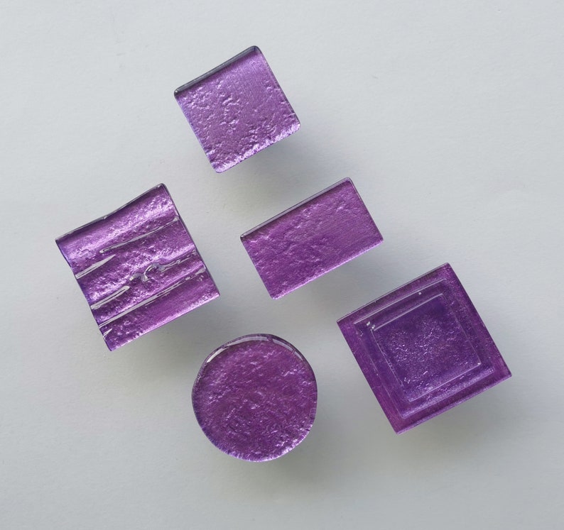 Fired glass cabinet knobs in sparkly purple made of round, square and rectangular glass pieces attached over a metal base. Slightly textured glass furniture handles with rounded edges.