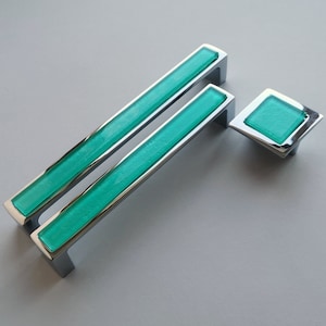 Peut inclure: Deux poignées de tiroir en chrome avec un insert en verre turquoise et un seul bouton en verre turquoise. Les poignées sont rectangulaires et le bouton est carré.