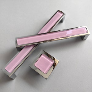 May include: Three cabinet pulls with a chrome finish and pink glass inserts. The pulls are in different sizes, with two long pulls and one square pull.