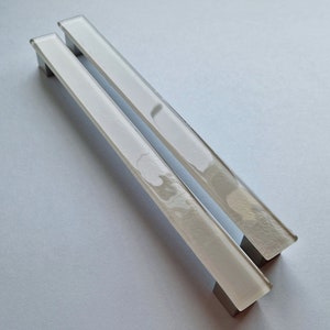 May include: Two white glass cabinet door pulls with a brushed nickel finish.