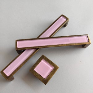 Peut inclure: Trois poignées de porte avec un insert en verre rose et un cadre en laiton. Les poignées sont en forme de rectangle et de carré.