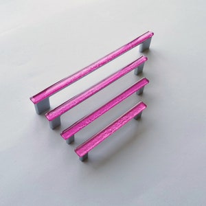 Fired glass cabinet pulls in sparkly bright pink made of fine glass sticks attached over a metal base. Slightly textured glass furniture handles with rounded edges.