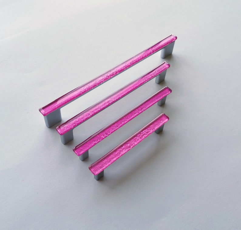 Fired glass cabinet pulls in sparkly bright pink made of fine glass sticks attached over a metal base. Slightly textured glass furniture handles with rounded edges.