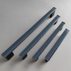 Op de afbeelding: Vier grijze glazen kastdeurgrepen in verschillende lengtes. De grepen hebben een glad, licht gebogen oppervlak.