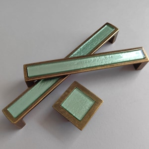 May include: Two antique brass cabinet pulls with a light green glass insert. A matching square knob with a light green glass insert is also shown.