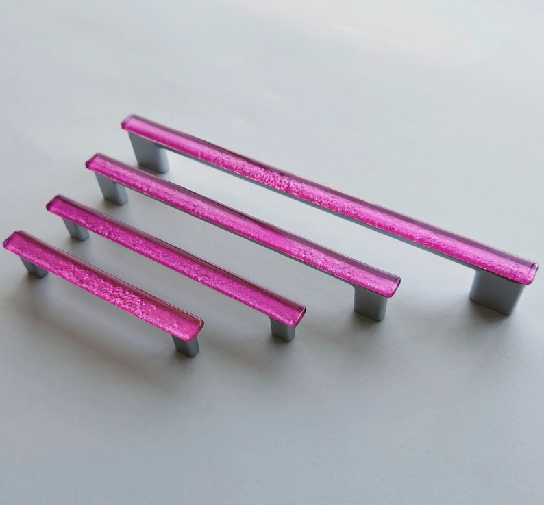 Fired glass cabinet pulls in sparkly bright pink made of fine glass sticks attached over a metal base. Slightly textured glass furniture handles with rounded edges.