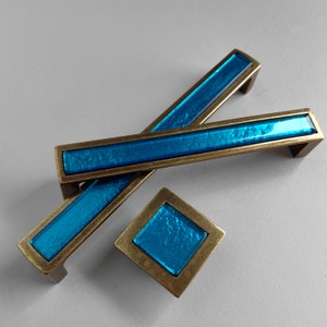 May include: Two blue and brass cabinet pulls with a matching smaller blue and brass knob. The pulls are rectangular with a blue glass insert and the knob is square with a blue glass insert.
