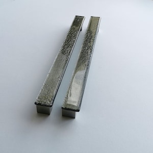 May include: Two silver-toned rectangular cabinet pulls with a textured surface. The pulls have a modern design and are set against a white background. The pulls are approximately 8 inches long.