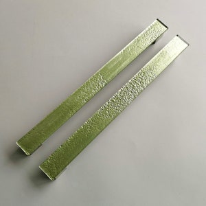 May include: Two long, green, textured metal cabinet pulls. The pulls are rectangular in shape and have a slightly rounded edge.