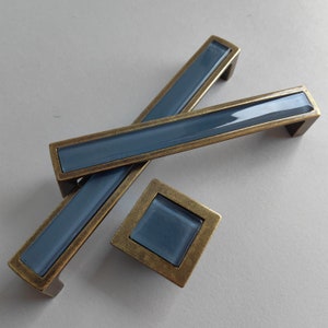 Peut inclure: Trois poignées de porte avec un insert en verre bleu et une finition en laiton. Les poignées sont en forme de rectangle et de carré.