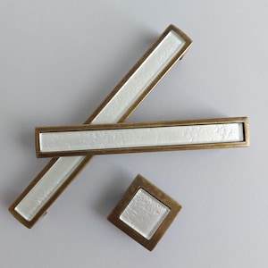 May include: Three antique brass cabinet pulls with a white, textured glass insert. The pulls are in the shape of a rectangle and a square.