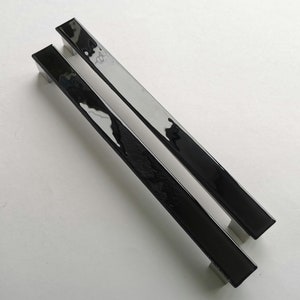 Puede incluir: Dos tiradores de puerta de armario negros con acabado en níquel cepillado. Los tiradores son de forma rectangular y tienen un diseño elegante y moderno.