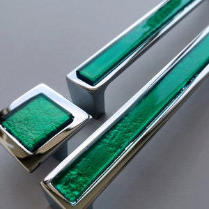 May include: Two chrome cabinet pulls with green glass inserts. The smaller pull is square shaped and the larger pull is rectangular.
