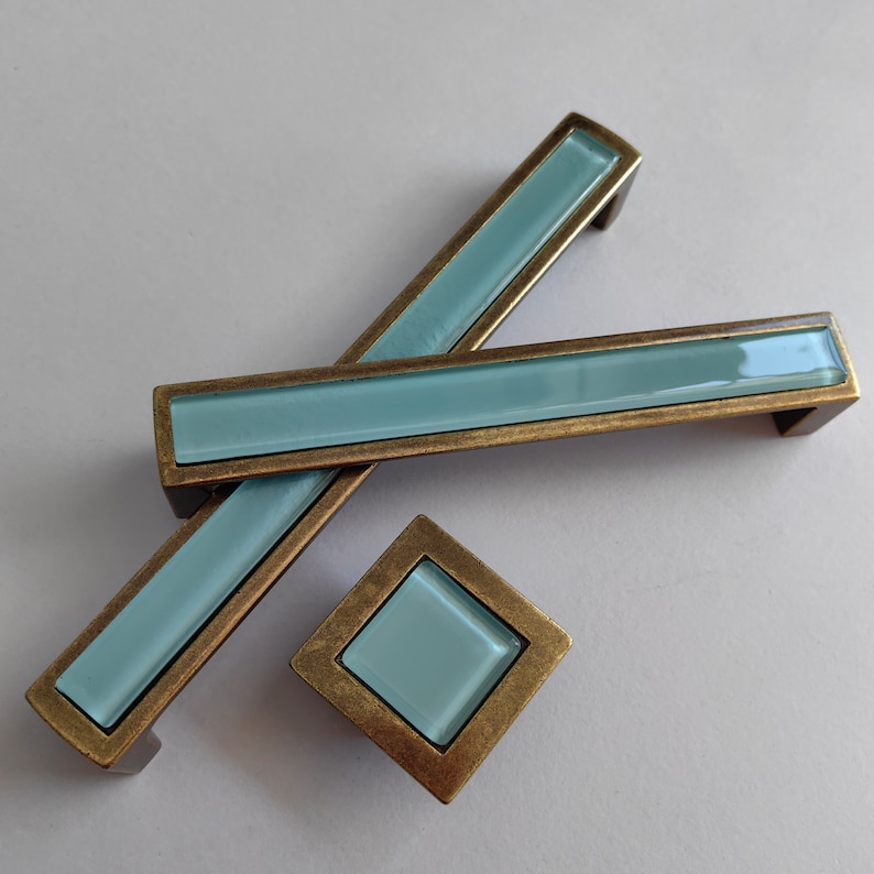 May include: Set of three cabinet pulls with a light blue glass insert and a brass finish. The pulls are in different sizes and shapes.
