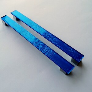 Set of two sparkly bright blue fired glass fridge pulls made of long glass sticks attached over a silvery metal base. Slightly textured glass furniture handles with rounded edges.