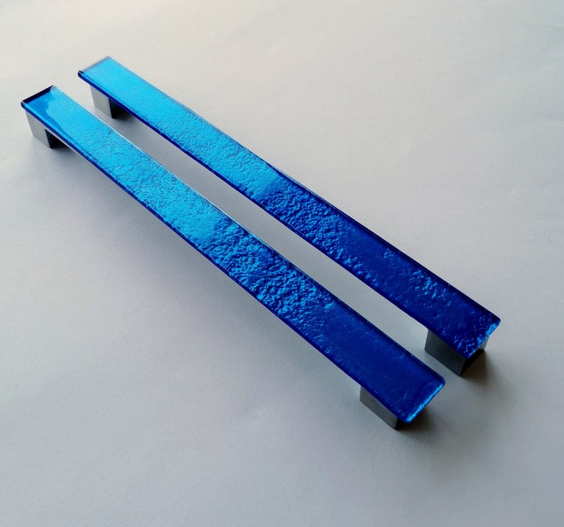 Set of two sparkly bright blue fired glass fridge pulls made of long glass sticks attached over a silvery metal base. Slightly textured glass furniture handles with rounded edges.