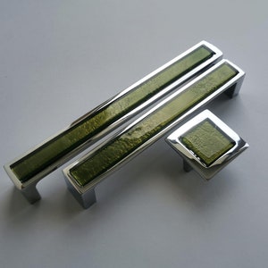 May include: Three cabinet pulls with a chrome finish and green glass inserts. The pulls are rectangular and the smallest pull is square.