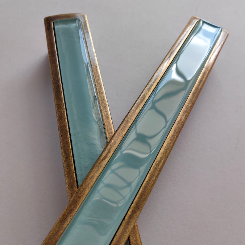 May include: Two cabinet pulls with a brass finish and a light blue glass insert.