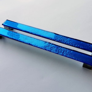 May include: Two blue glass cabinet door pulls with a textured finish. The pulls are rectangular and have a silver metal base.