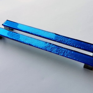 Set of two sparkly bright blue fired glass fridge pulls made of long glass sticks attached over a silvery metal base. Slightly textured glass furniture handles with rounded edges.