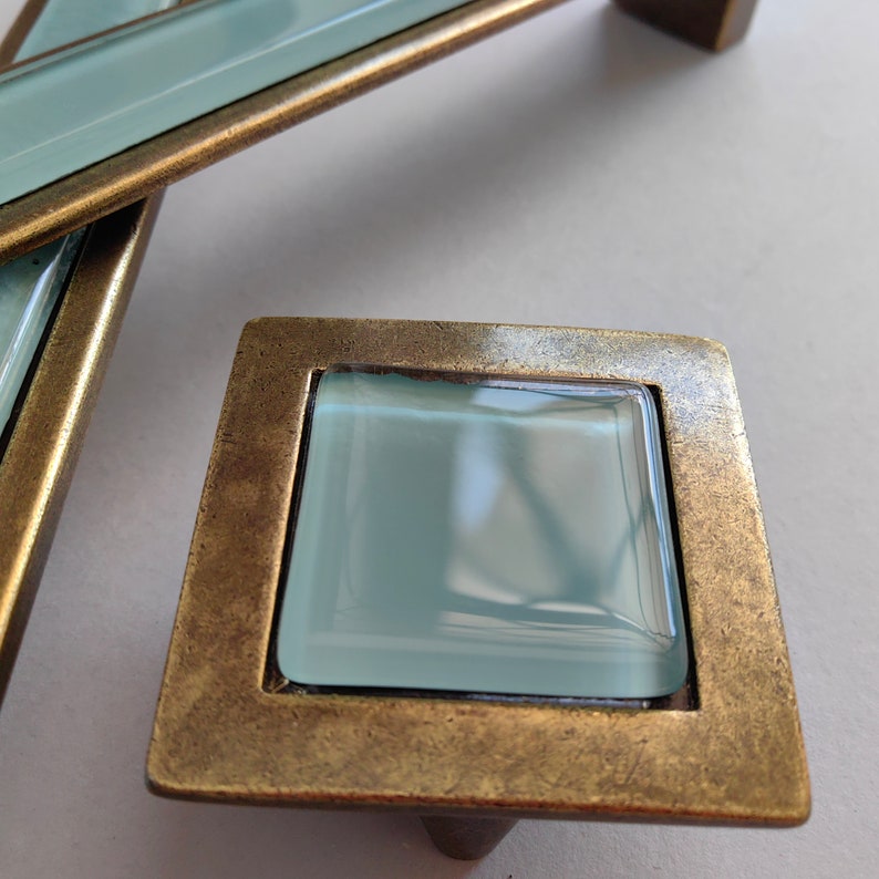 May include: A square cabinet knob with a brushed brass finish and a light blue glass insert.