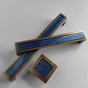 May include: Three blue and gold cabinet pulls with a textured finish. The pulls are in the shape of a rectangle with rounded edges.