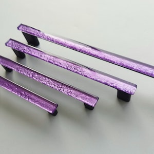 Fired glass cabinet pulls in sparkly purple made of fine glass sticks attached over a metal base. Slightly textured glass furniture handles with rounded edges.