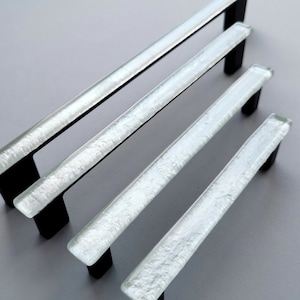 Fired glass cabinet pulls in metallic pearl white made of fine glass sticks attached over a metal base. Slightly textured glass furniture handles with rounded edges.