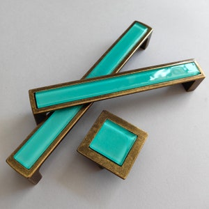 May include: Set of three cabinet hardware pieces: two rectangular pulls and one square knob. Each piece features a rectangular or square turquoise glass insert set within a bronze-toned metal frame. The pulls are approximately 5 inches long.