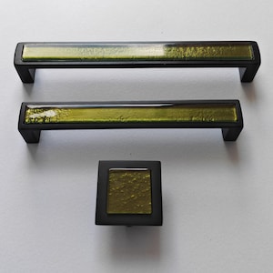 Peut inclure: Ensemble de trois pièces de quincaillerie d'armoire : deux poignées rectangulaires et un bouton carré. La quincaillerie est noire avec un insert rectangulaire en verre vert olive texturé. Les poignées mesurent environ 15 cm de long.
