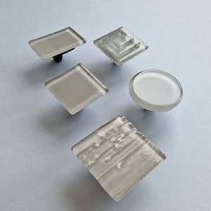 May include: Five different glass cabinet knobs in various shapes and sizes. The knobs are all white and have a frosted finish.