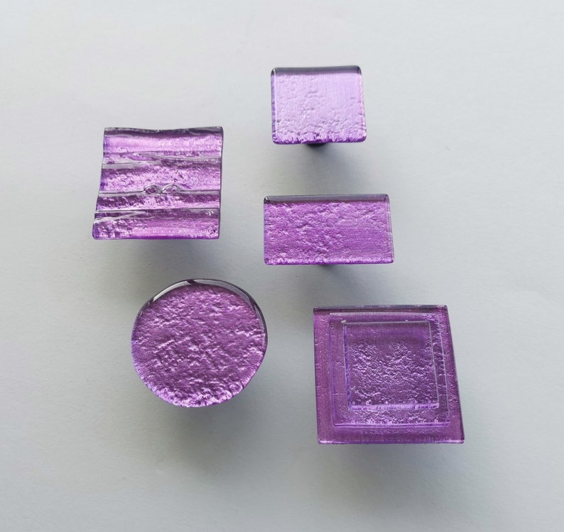 Fired glass cabinet knobs in sparkly purple made of round, square and rectangular glass pieces attached over a metal base. Slightly textured glass furniture handles with rounded edges.