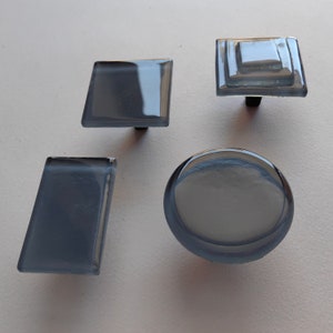 Può includere: Quattro pomelli per armadio in vetro di diverse forme e dimensioni. I pomelli sono tutti di colore grigio chiaro con una finitura leggermente opaca.