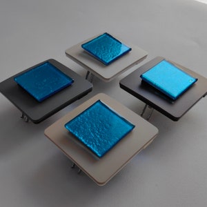 May include: Four square light switch covers with a blue glass insert. The covers are in two different colours, white and grey.