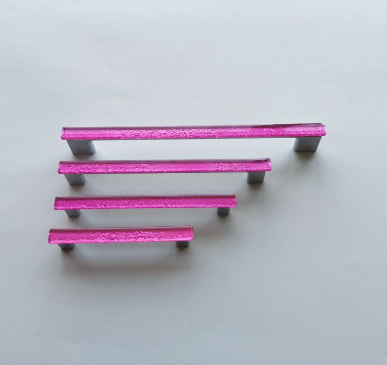 Fired glass cabinet pulls in sparkly bright pink made of fine glass sticks attached over a metal base. Slightly textured glass furniture handles with rounded edges.