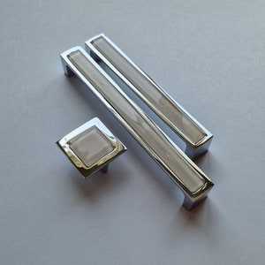 Peut inclure: Deux poignées de tiroir en chrome avec un insert en céramique blanche et un bouton carré en chrome avec un insert en céramique blanche.
