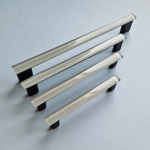 Pode incluir: Quatro puxadores de armário prateados com bases pretas, dispostos em ordem decrescente de tamanho.