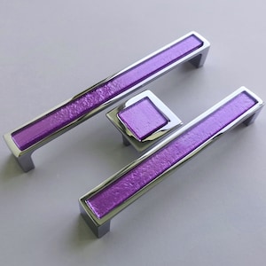 Può includere: Tre tiretti per cassetti in cromo e viola con finitura testurizzata. I tiretti hanno la forma di un rettangolo con bordi arrotondati.