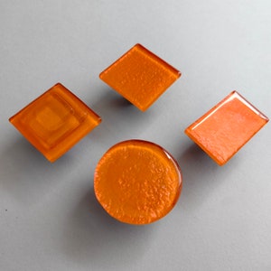 Peut inclure: Quatre boutons de cabinet en verre orange de formes différentes : un cercle, un losange, un carré et un rectangle. Les boutons ont une surface texturée.