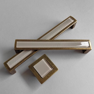 May include: Three antique brass cabinet pulls with a frosted glass insert. The pulls are in the shape of a rectangle with rounded corners. The smaller pull is square shaped.