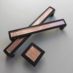 Può includere: Un set di ferramenta nera per mobili, tra cui due maniglie rettangolari e un pomello quadrato. Ogni pezzo presenta un centro strutturato color oro rosa incorniciato in nero. Adatto per mobili e decorazioni per la casa.