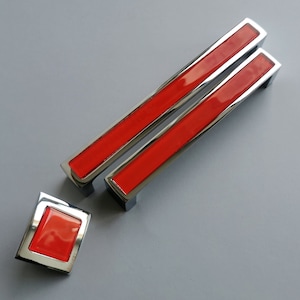 May include: Two red and chrome cabinet pulls with a matching red and chrome square knob.
