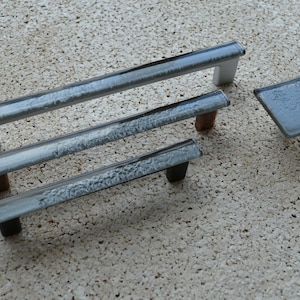 May include: A set of cabinet hardware, including three silver-toned bar pulls and a square knob. The pulls have a frosted glass-like appearance with varying base colors: white, brown, and black. The knob has a similar frosted design.